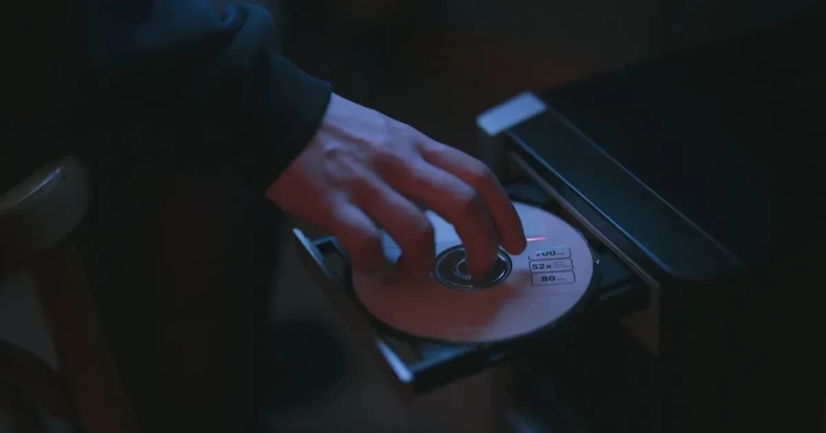 A hand inserting a CD into a computer drive, highlighting cyber security themes.