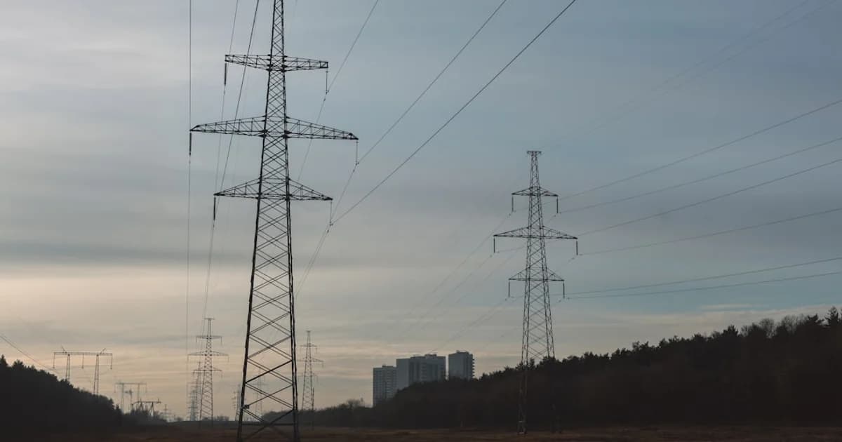 Power lines stretch across a field towards distant buildings.