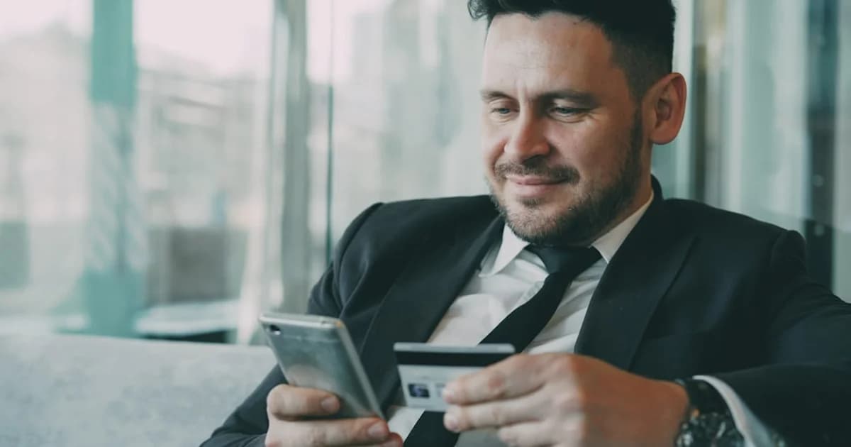 Man in suit using smartphone and credit card.