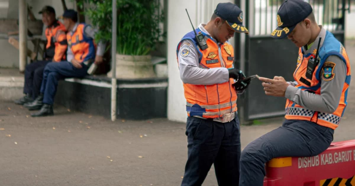 Two traffic officers in orange vests check their phones.
